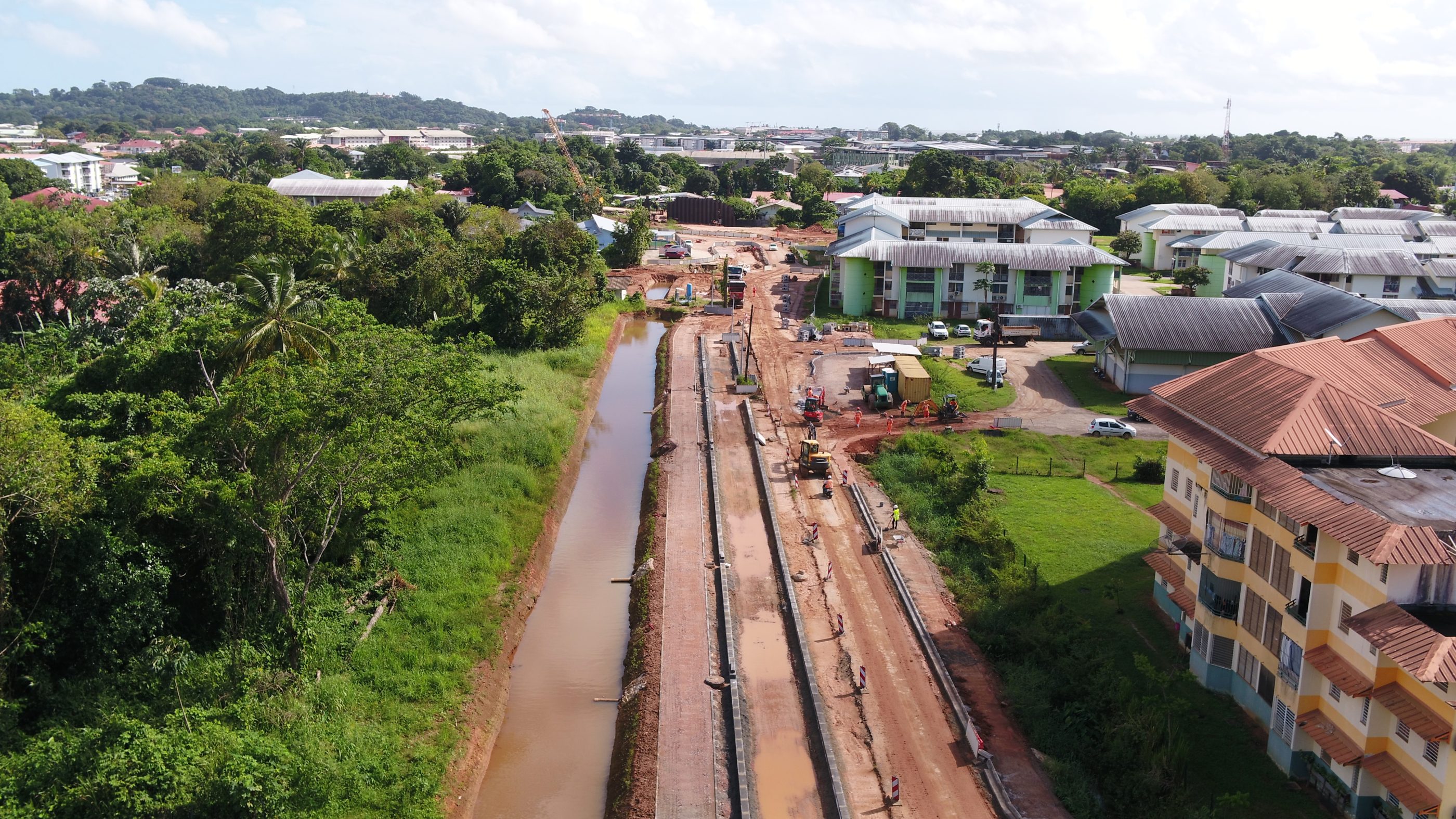 Chantier avec à gauche une forêt et à droite des immeubles d'habitation.